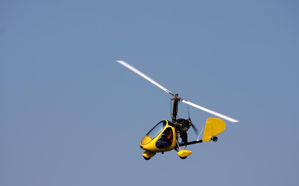 A yellow gyroplane climbing against a clear blue sky.